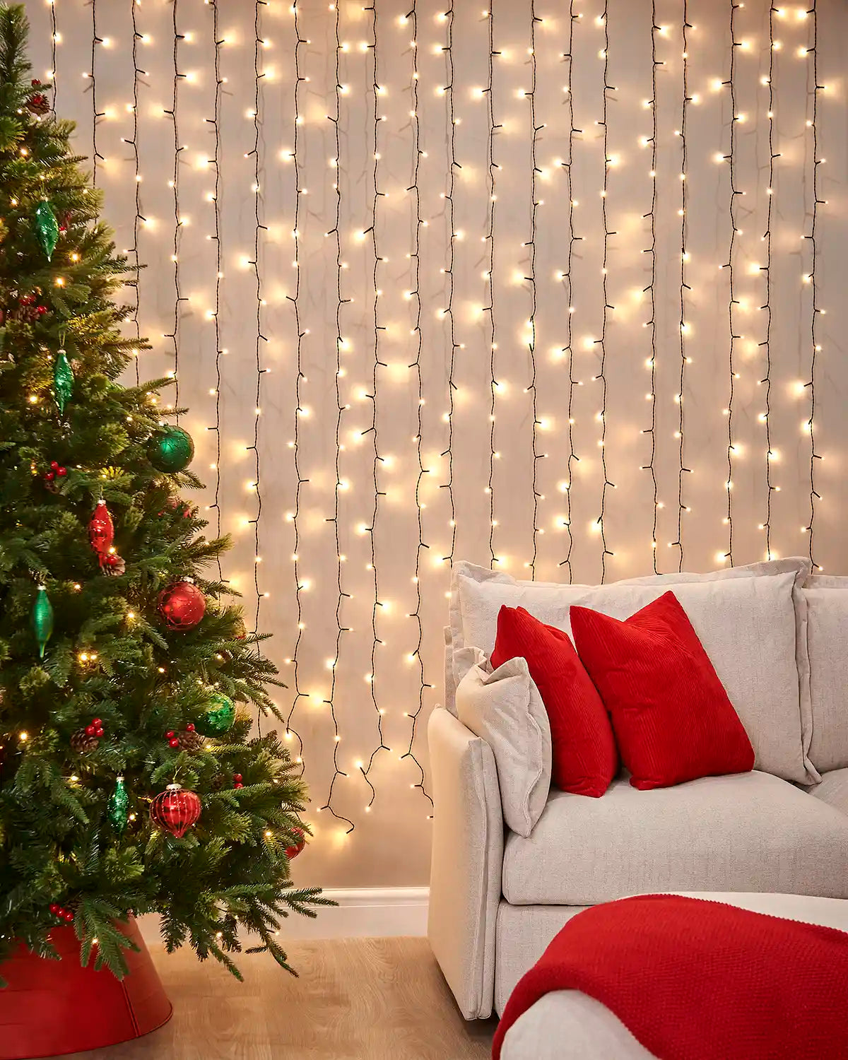 Warm white curtain lights on black cable displayed on a wall beside a Christmas tree and sofa.