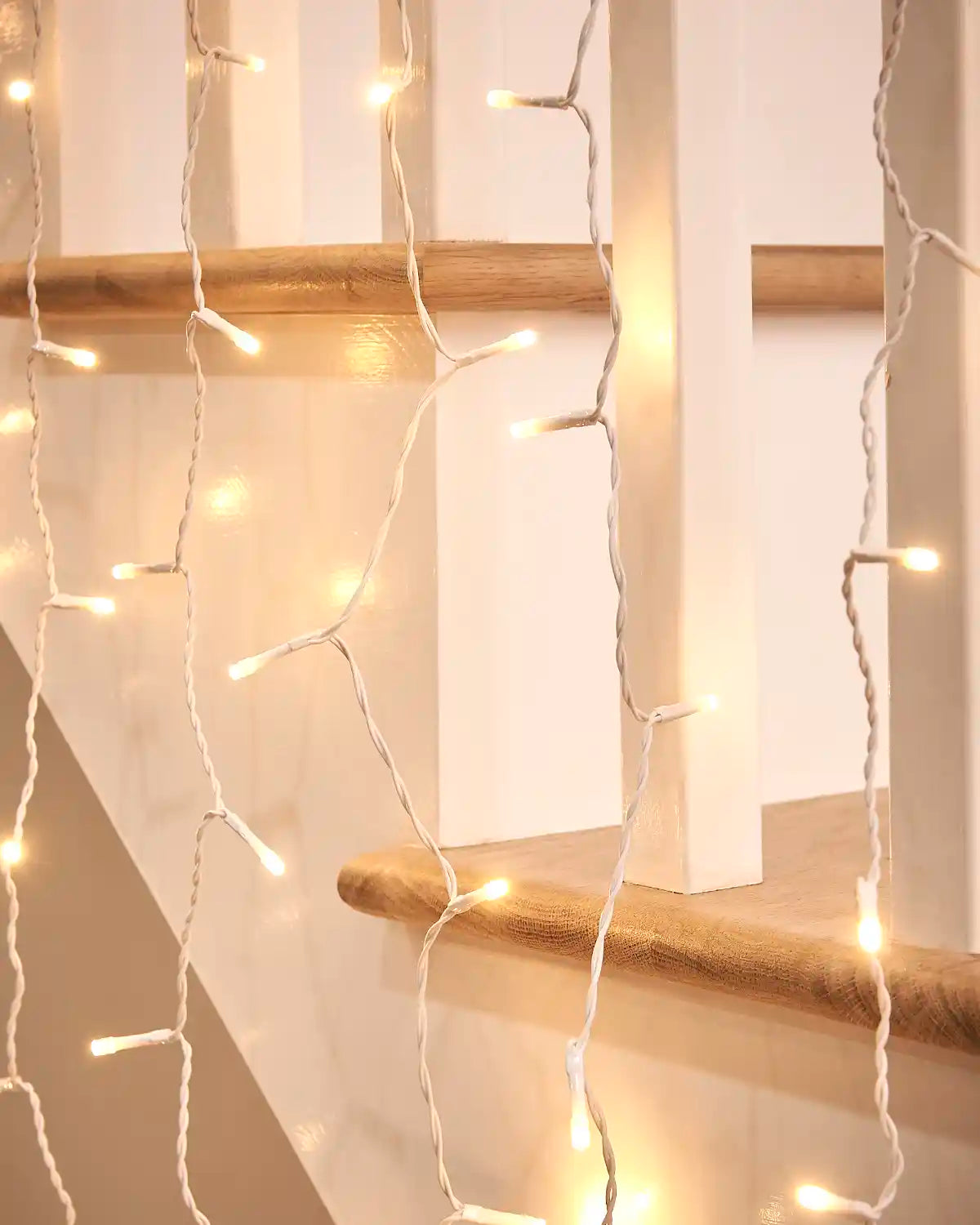 Close-up of warm white curtain lights on white cable hanging near a wooden stair rail.