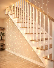 Warm white curtain lights on white cable hanging beside an indoor staircase.