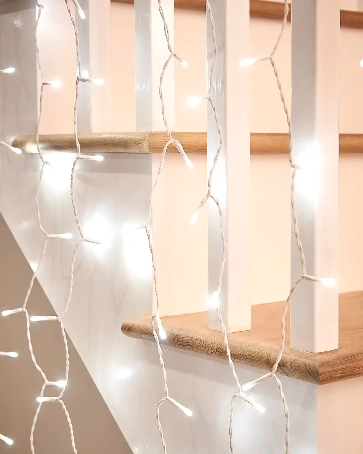 Close-up of white curtain lights on white cable hanging near a wooden stair rail.