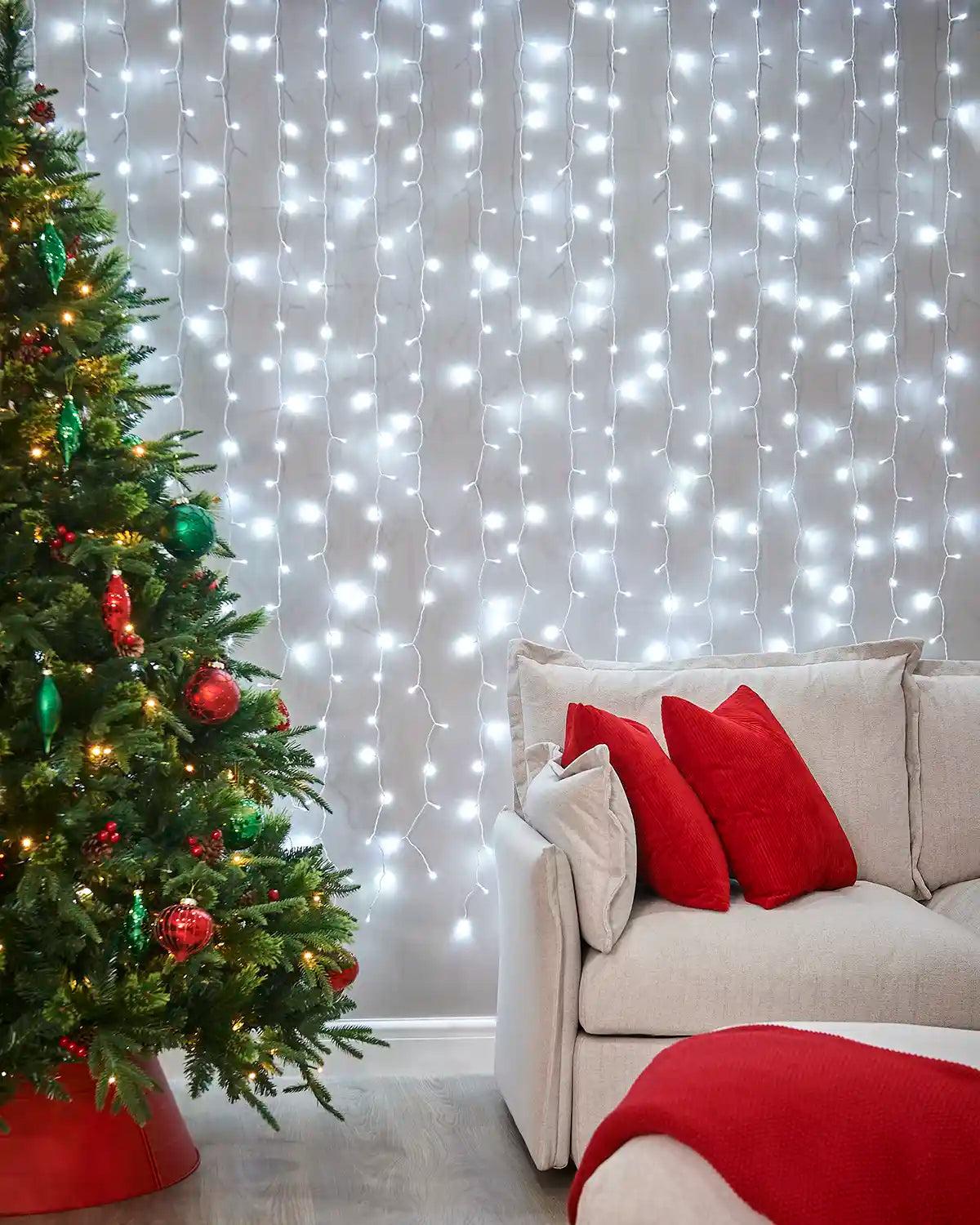 White curtain lights on white cable displayed on a wall behind a sofa and Christmas tree.