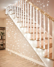 White curtain lights on white cable hanging beside an indoor staircase.