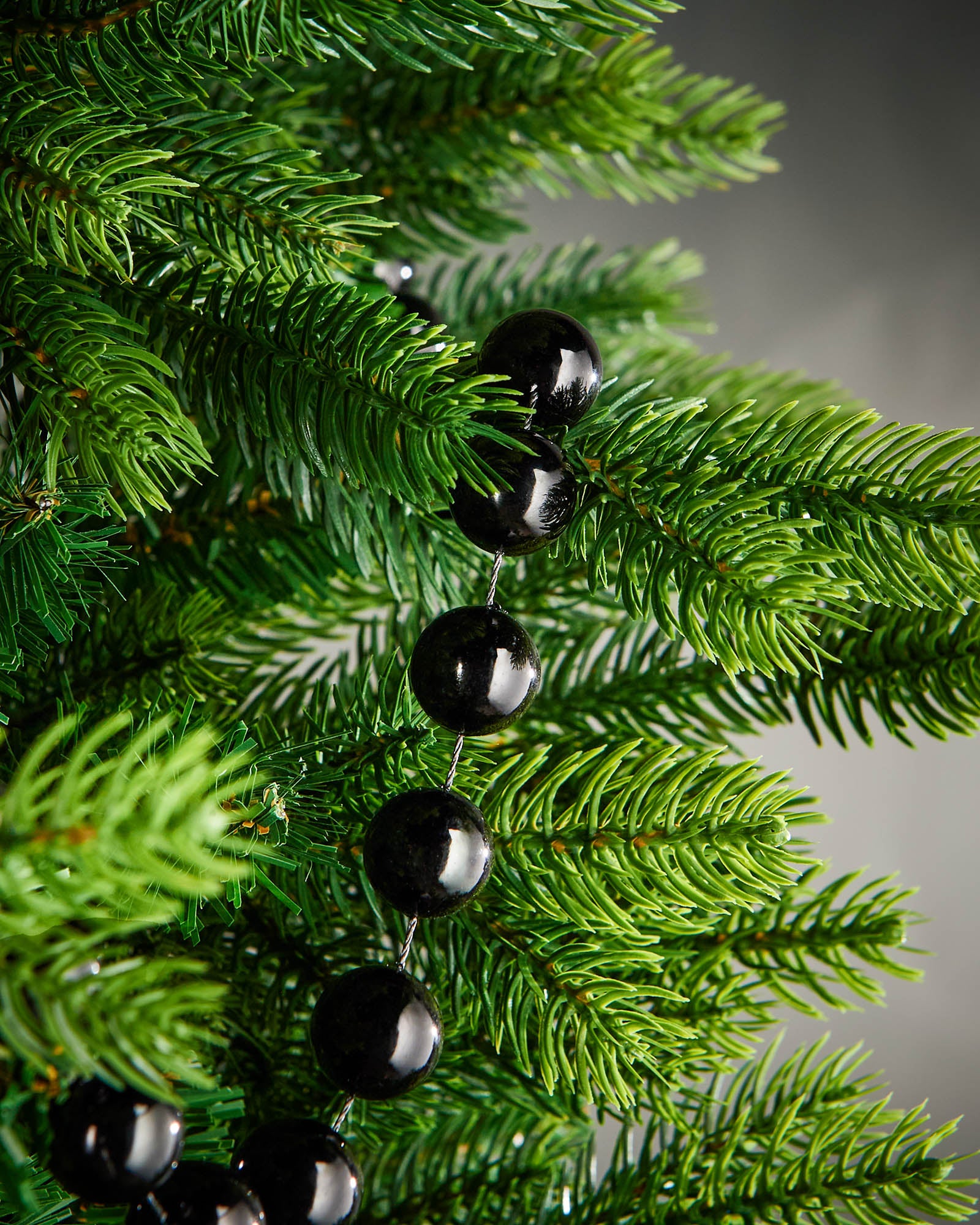 Detail of black oversized beaded garland woven through green Christmas tree branches.