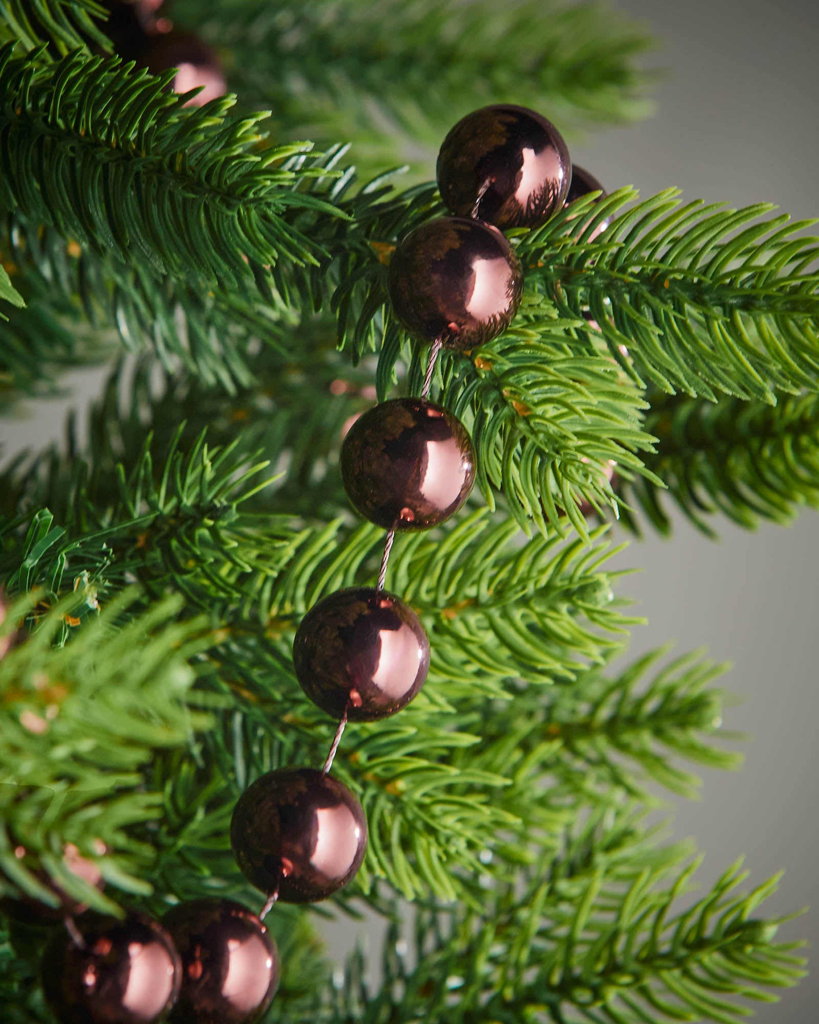 Detail of burgundy oversized beaded garland woven through green Christmas tree branches.