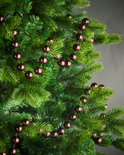 2.7m burgundy oversized beaded garland draped through green Christmas tree branches.
