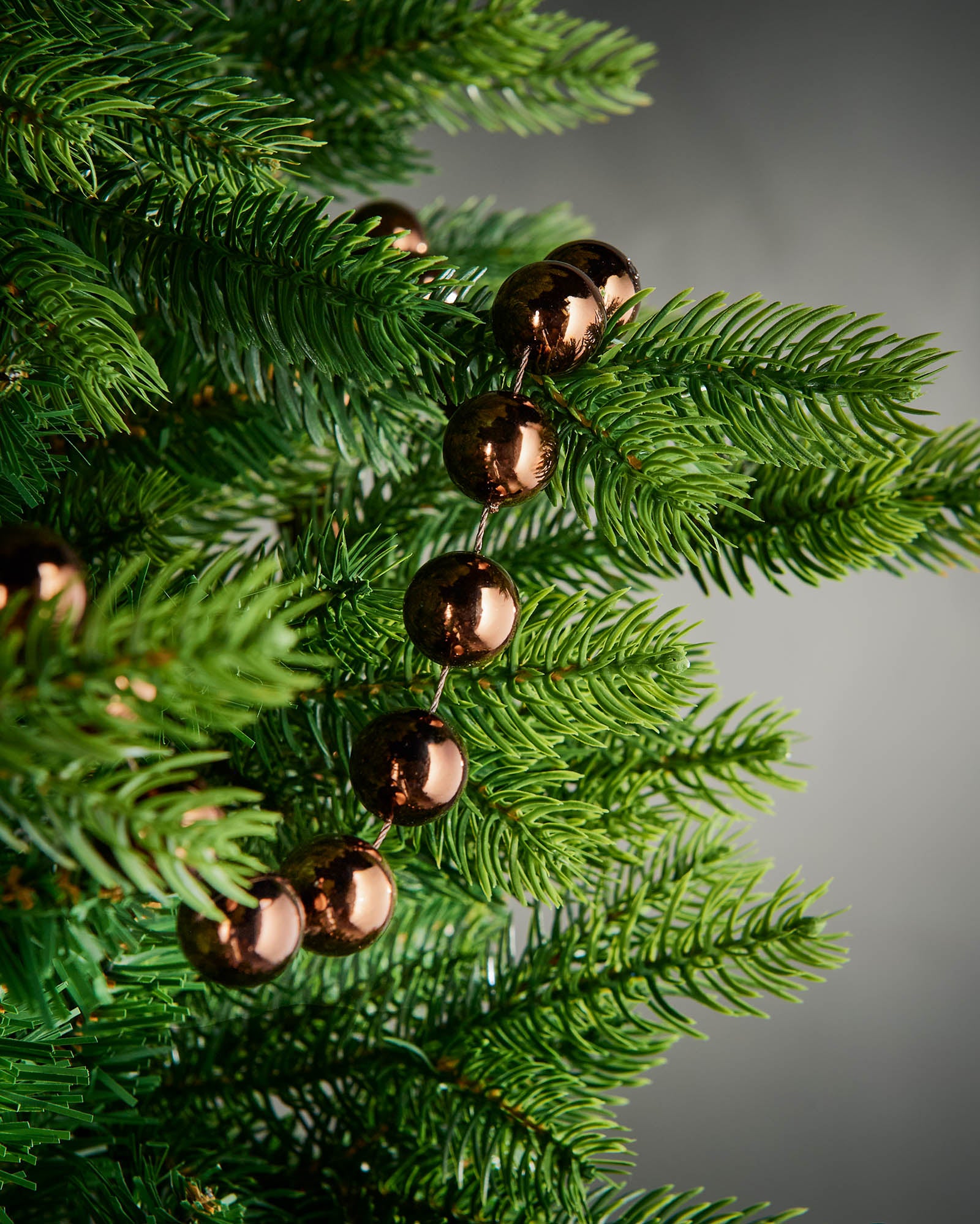 Detail of espresso oversized beaded garland woven through green Christmas tree branches.