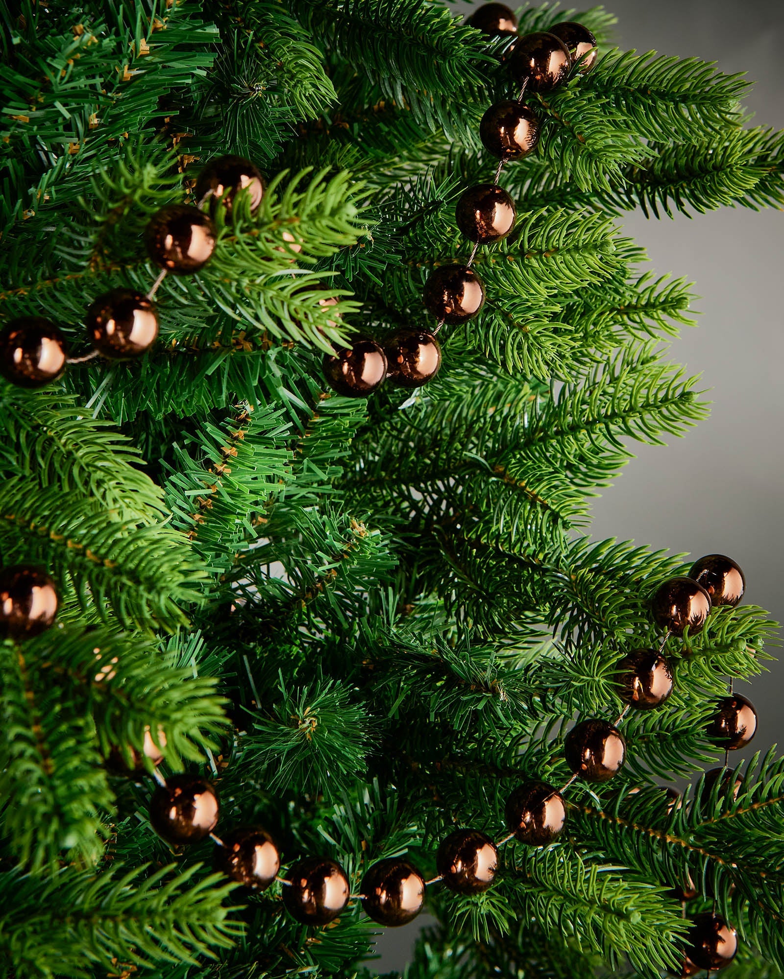 2.7m espresso oversized beaded garland draped through green Christmas tree branches.