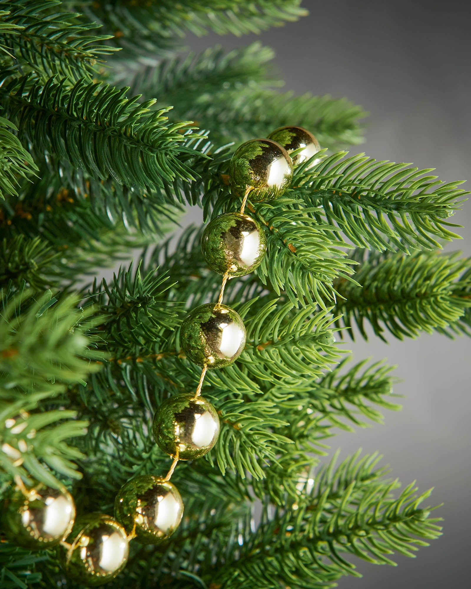Detail of gold oversized beaded garland woven through green Christmas tree branches.