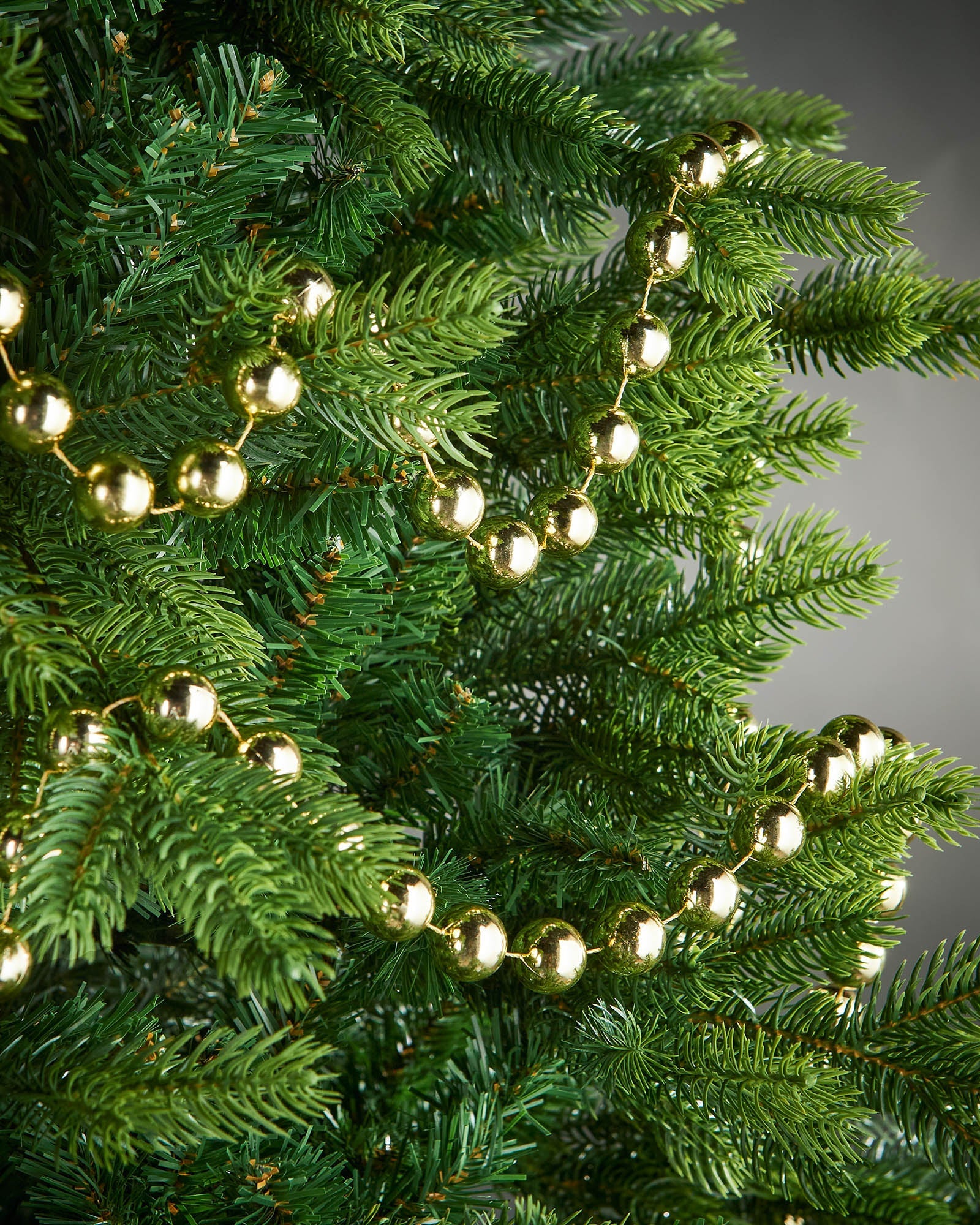 2.7m gold oversized beaded garland draped through green Christmas tree branches.