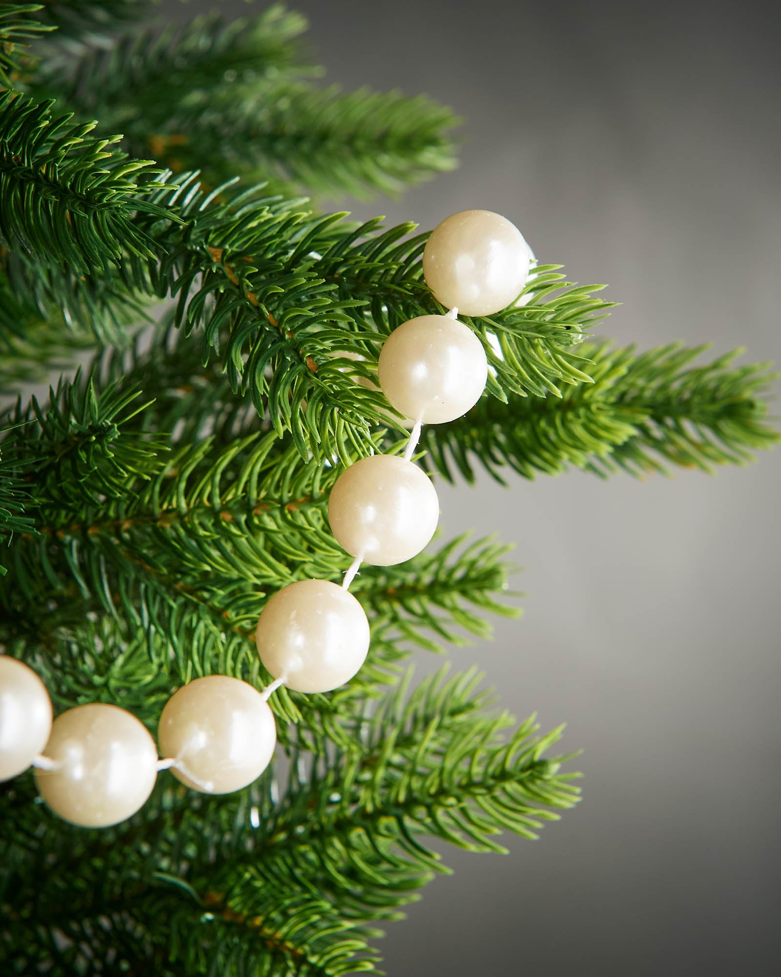 Detail of latte oversized beaded garland woven through green Christmas tree branches.