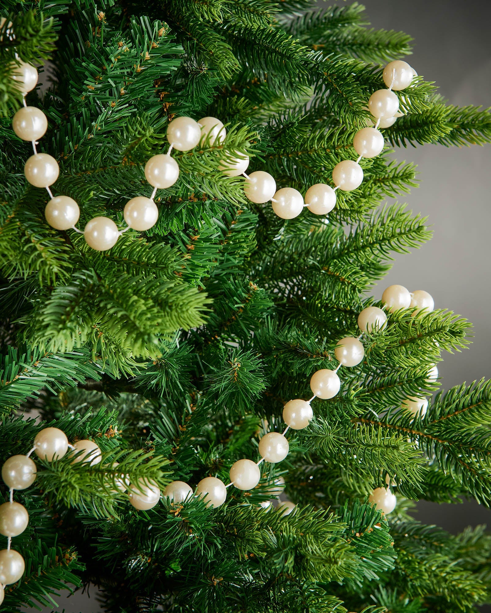 2.7m latte oversized beaded garland draped through green Christmas tree branches.
