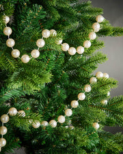 2.7m latte oversized beaded garland draped through green Christmas tree branches.