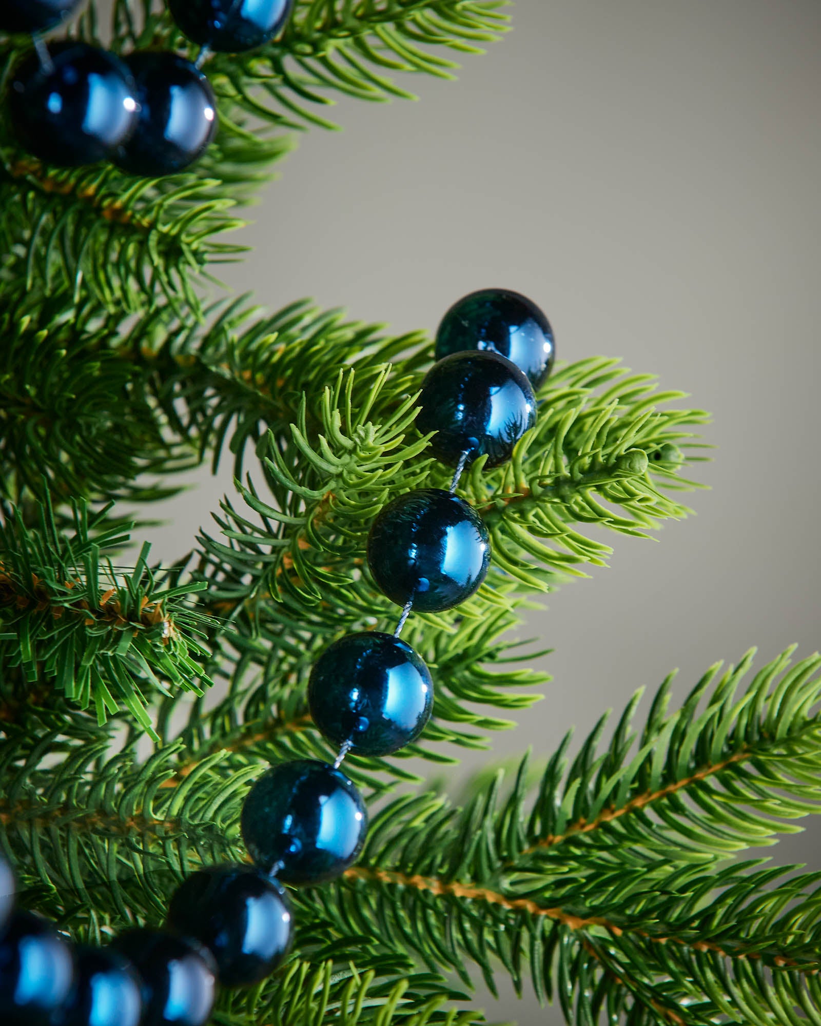Detail of navy blue oversized beaded garland woven through green Christmas tree branches.