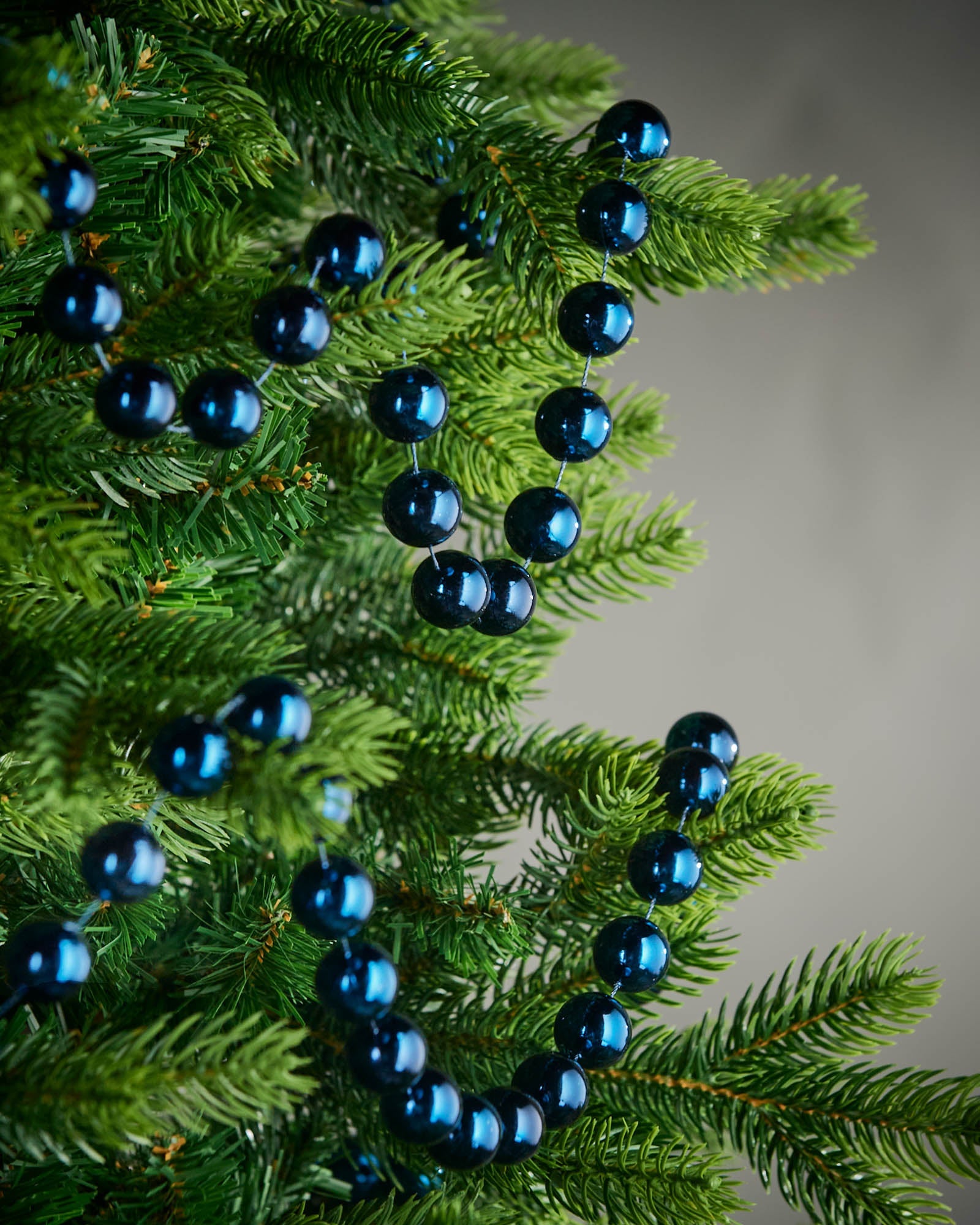 2.7m navy blue oversized beaded garland draped through green Christmas tree branches.