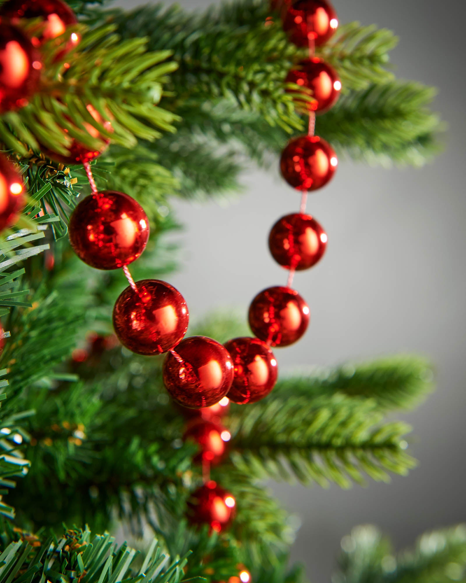 Detail of red oversized beaded garland woven through green Christmas tree branches.
