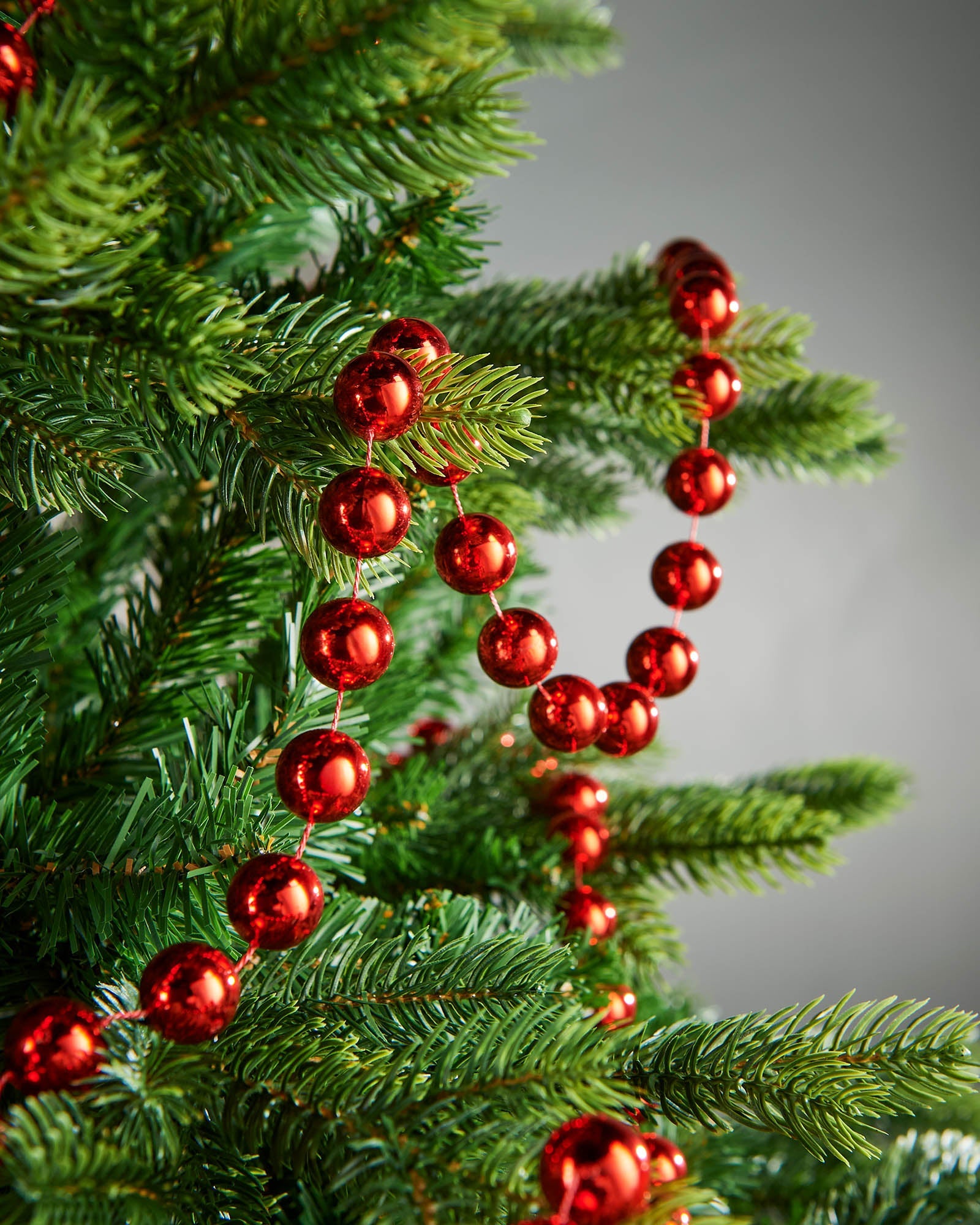 2.7m red oversized beaded garland draped through green Christmas tree branches.