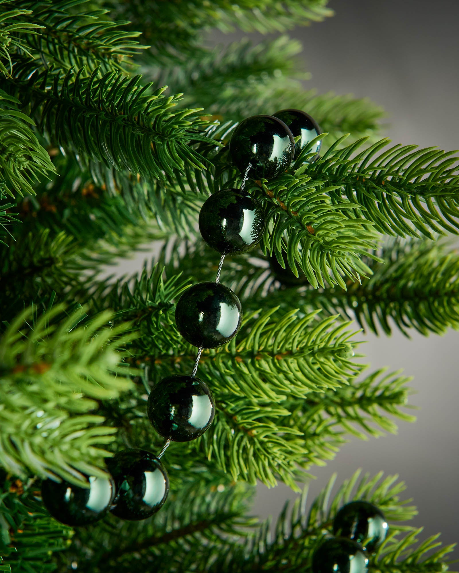 Detail of sage green oversized beaded garland woven through green Christmas tree branches.