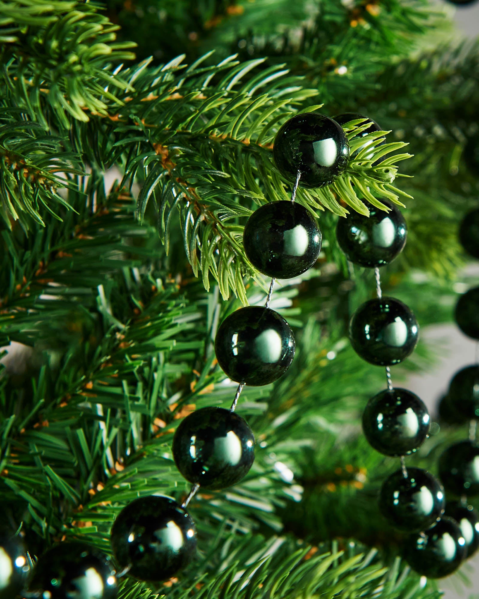 Close-up of glossy sage green beads on a 2.7m oversized garland displayed on a Christmas tree.