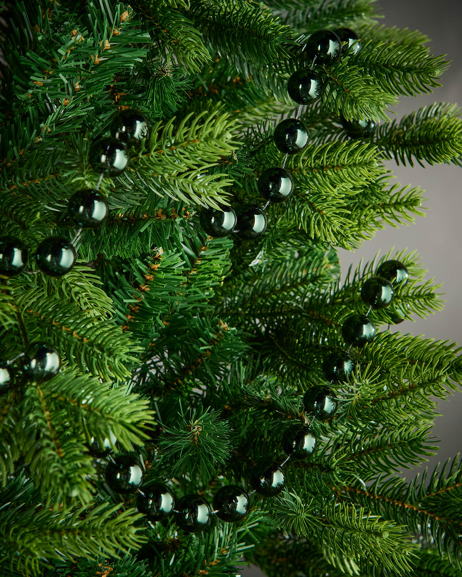 2.7m sage green oversized beaded garland draped through green Christmas tree branches.