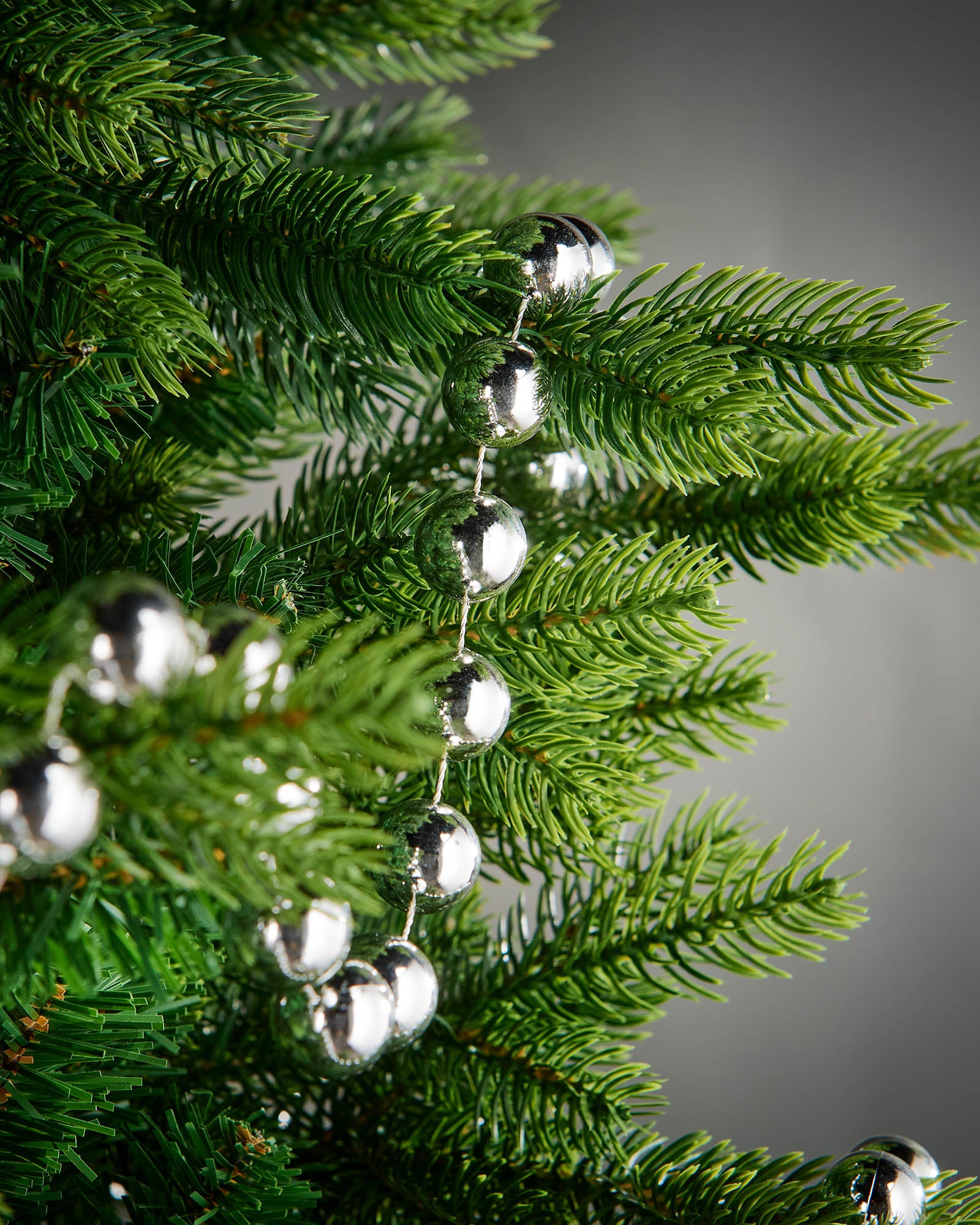 Detail of silver oversized beaded garland woven through green Christmas tree branches.