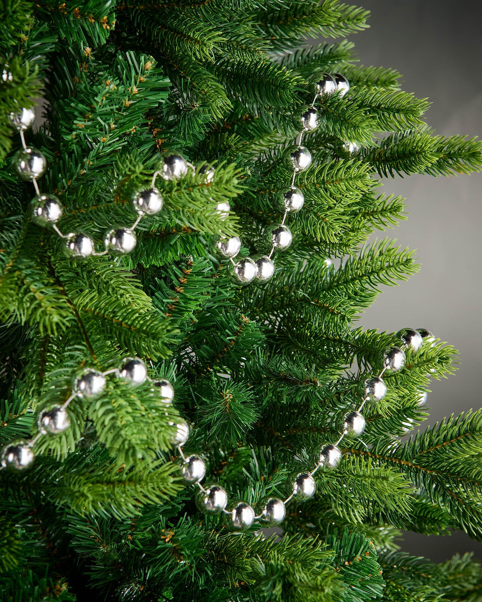 2.7m silver oversized beaded garland draped through green Christmas tree branches.