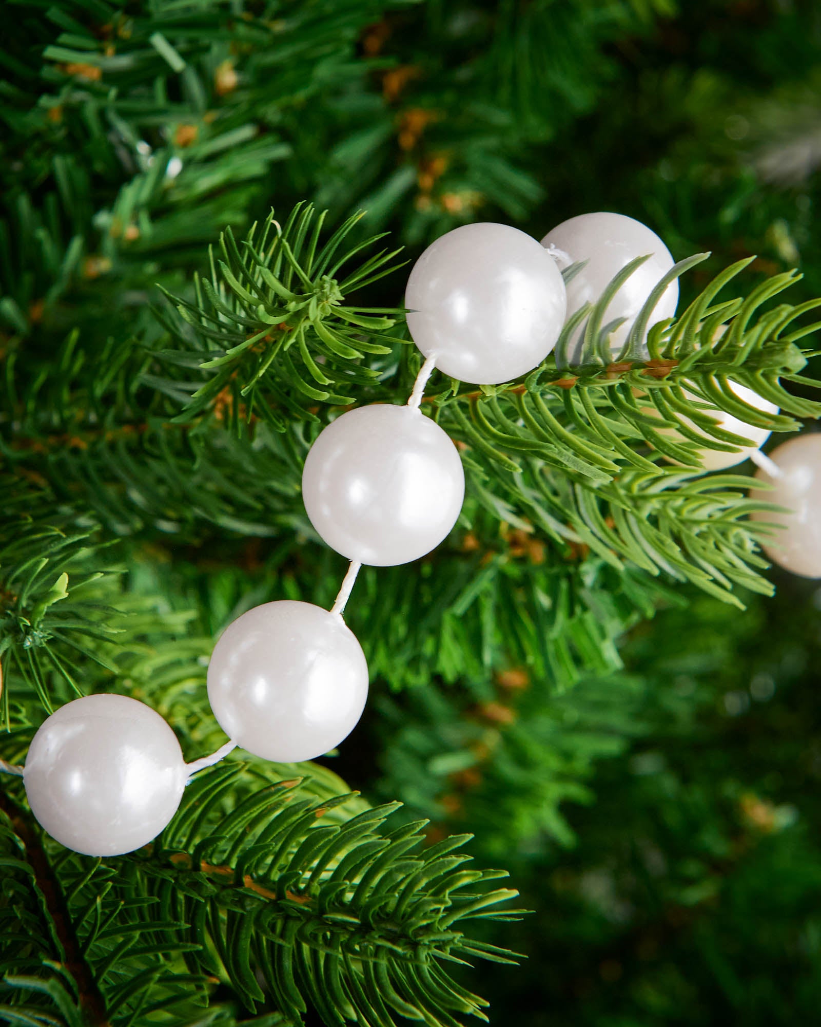 Detail of white oversized beaded garland woven through green Christmas tree branches.