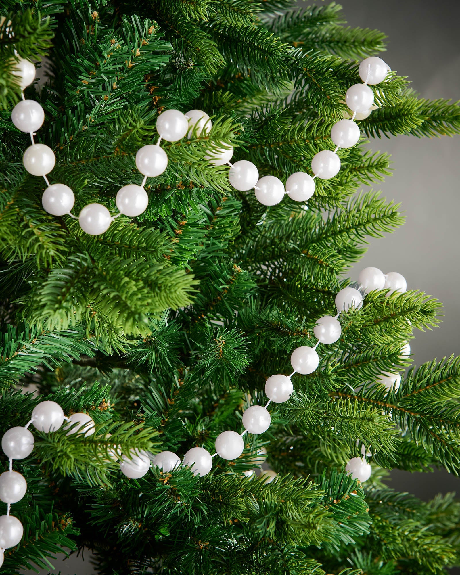2.7m white oversized beaded garland draped through green Christmas tree branches.