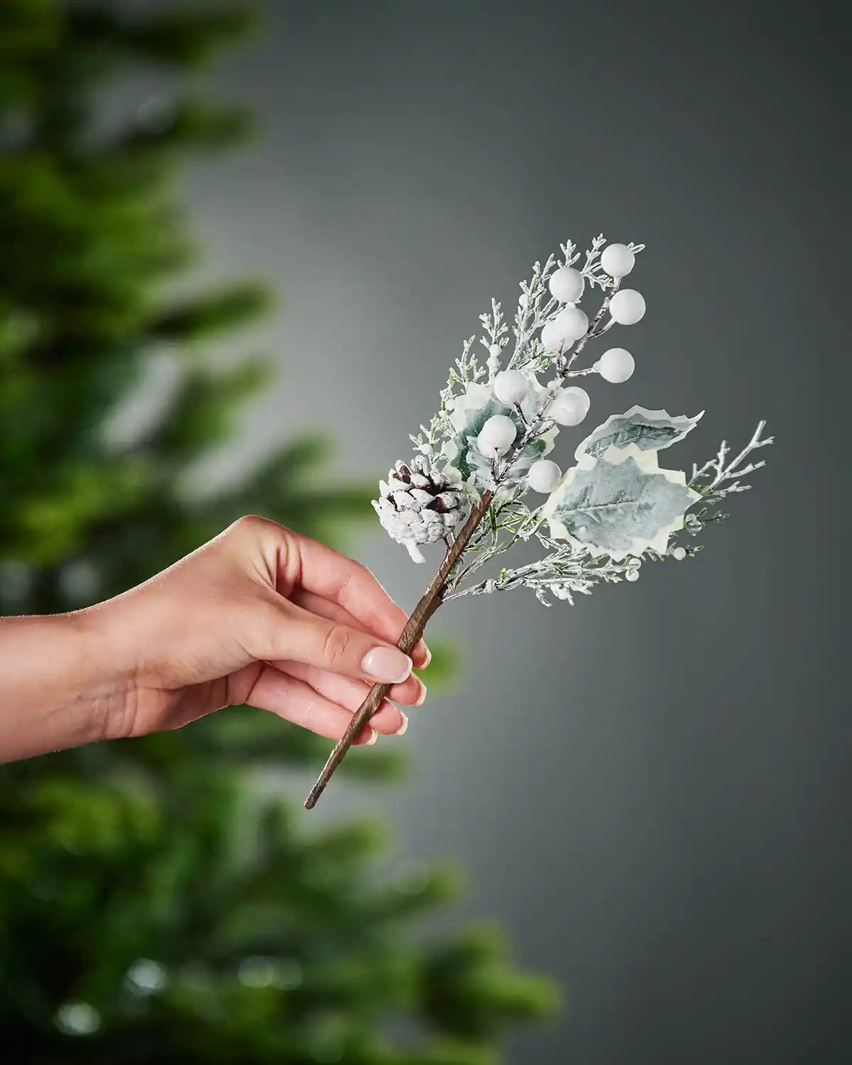 20 cm artificial frosted berries and pinecones pick held beside a Christmas tree