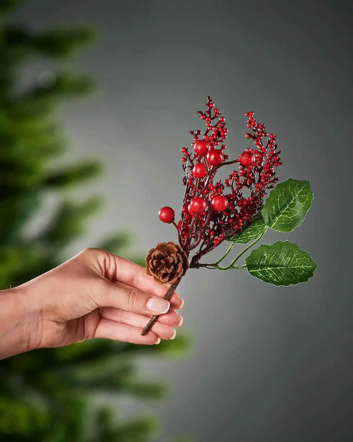 20 cm red artificial berries and pinecones tree pick held beside a Christmas tree