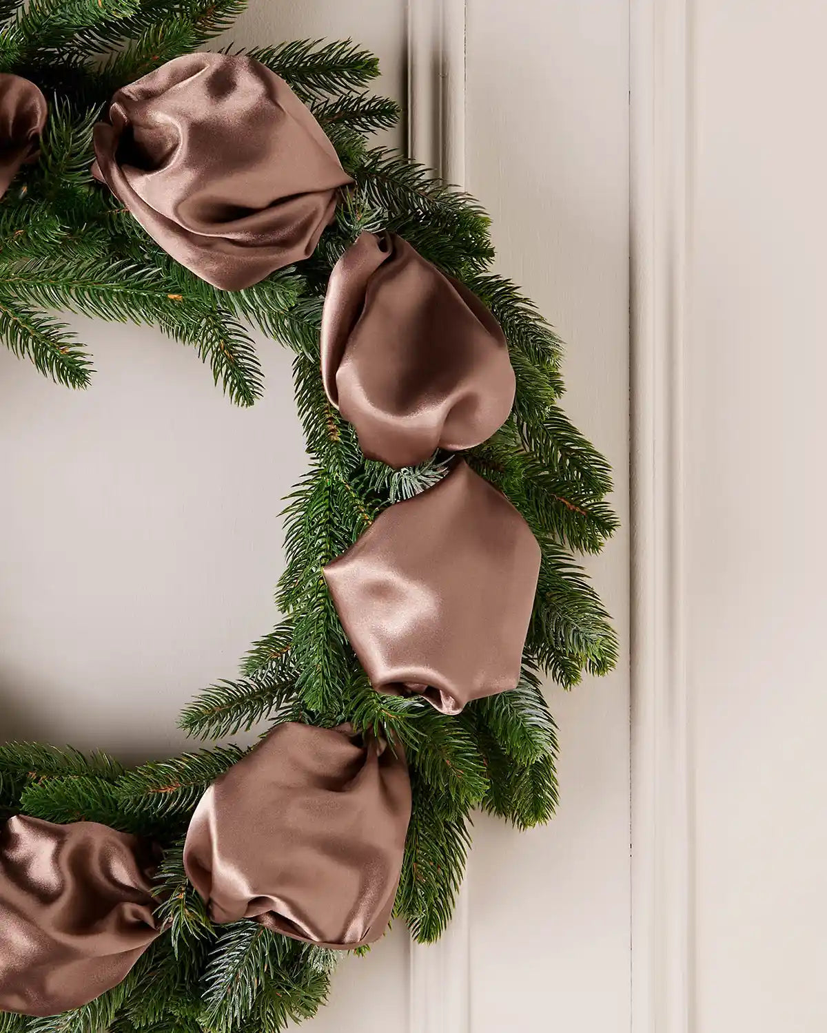 Mocha satin ribbon styled on a green Christmas wreath with soft folds and a satin finish.