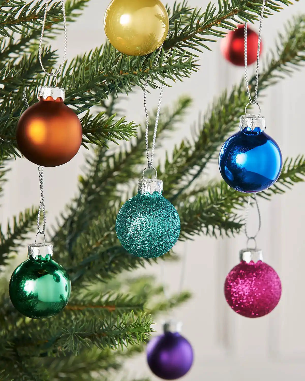 Small multi-coloured glass baubles styled on a Christmas tree