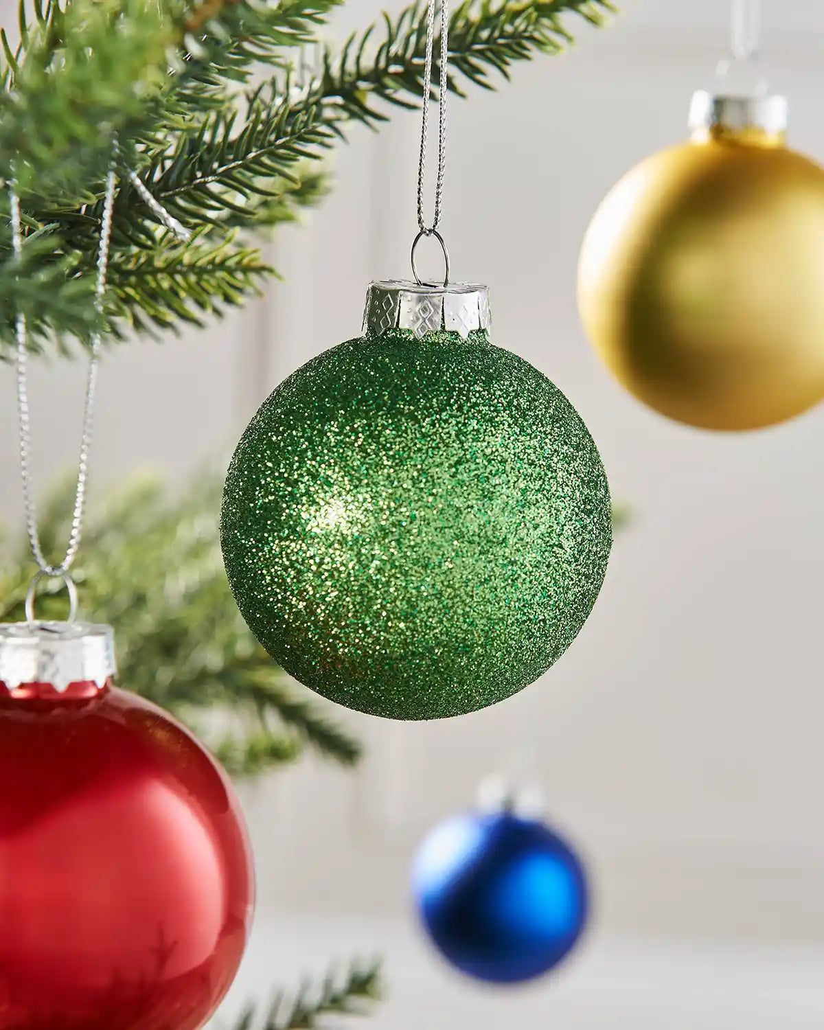 Close-up of a green glitter glass bauble hanging on a Christmas tree