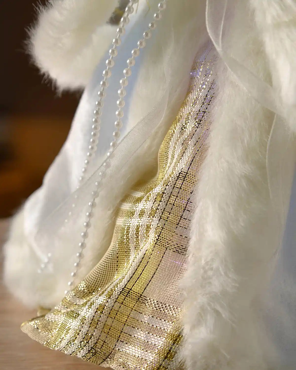 Close-up of the angel tree topper’s cream faux fur trim, pearl detail and gold patterned dress