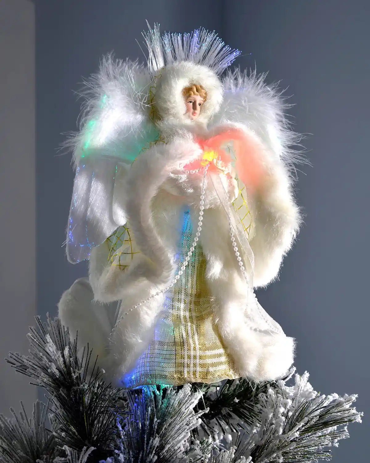 Cream and gold fibre optic angel tree topper placed on a snowy Christmas tree with coloured lights glowing