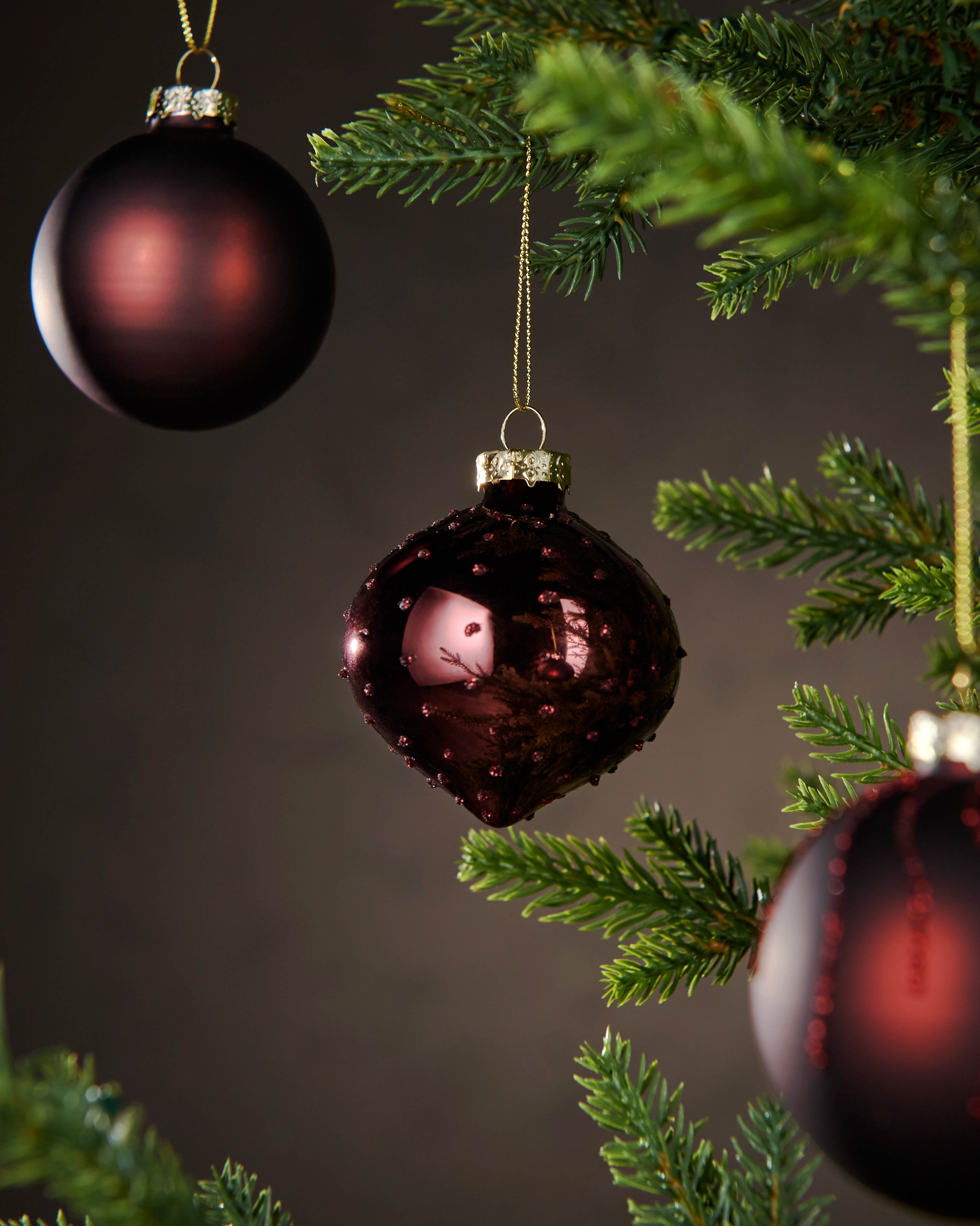 Red glass ornaments on a Christmas tree with a dark background