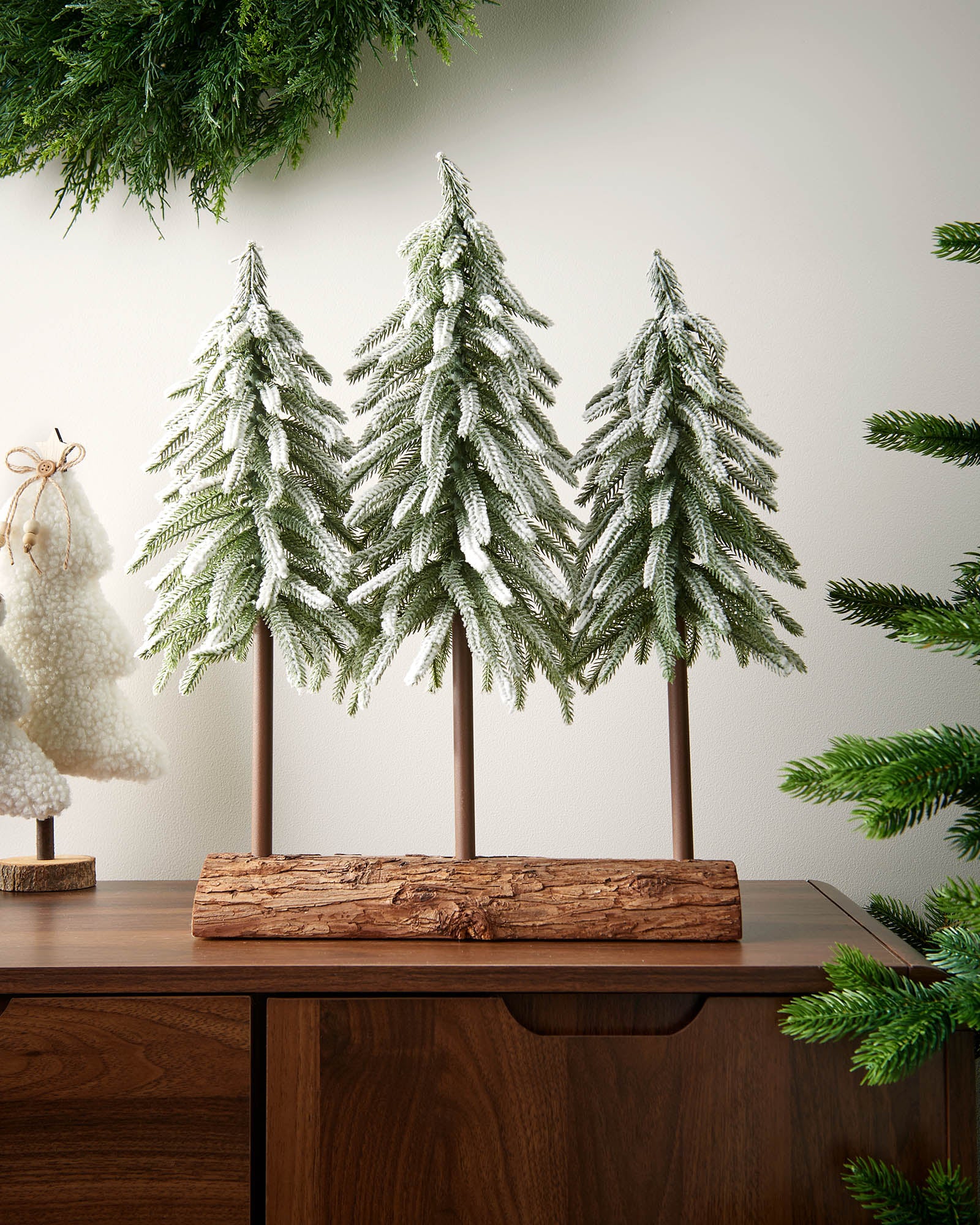 Decorative Christmas trees with snow on a wooden stand against a neutral background
