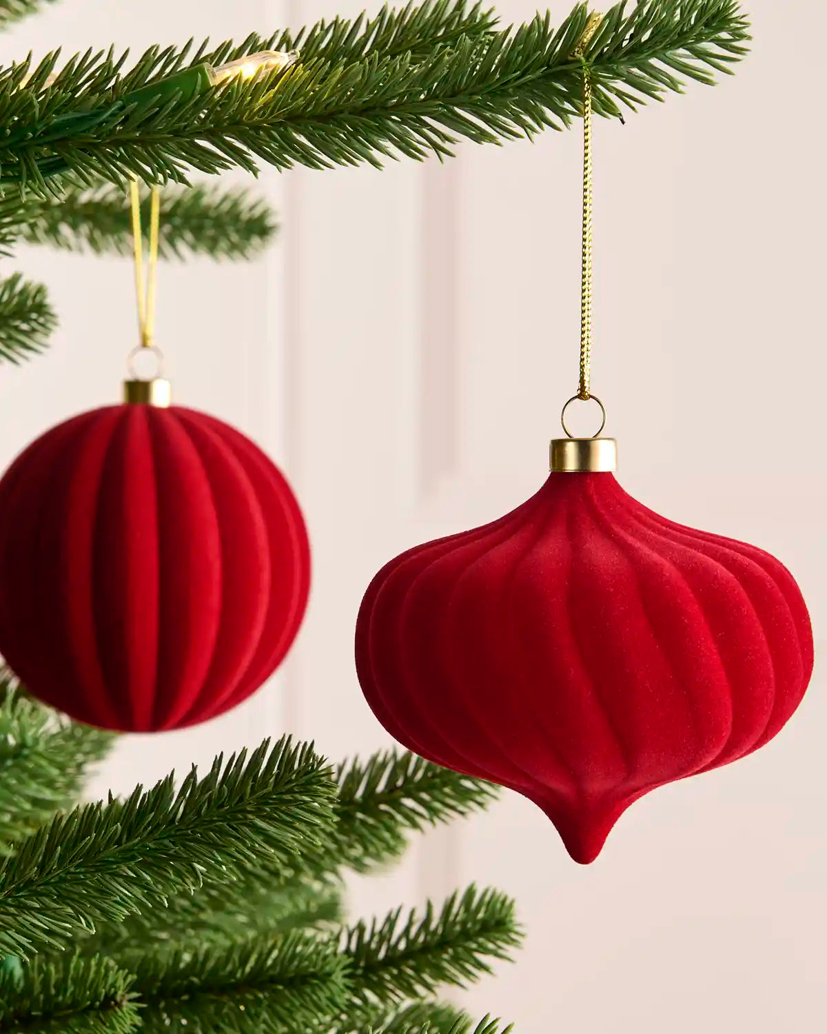 2 Red spiral and ribbed velvet baubles hanging on a Christmas tree against a light background