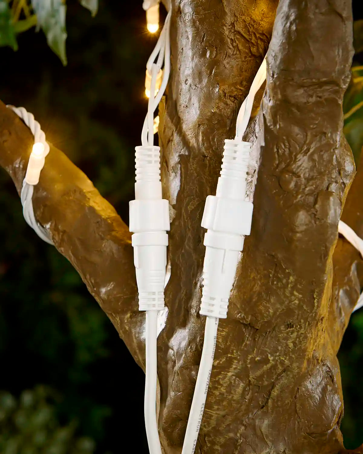 2 Screw cap connector points attached to tree with warm white LED string lights with a blurry garden background