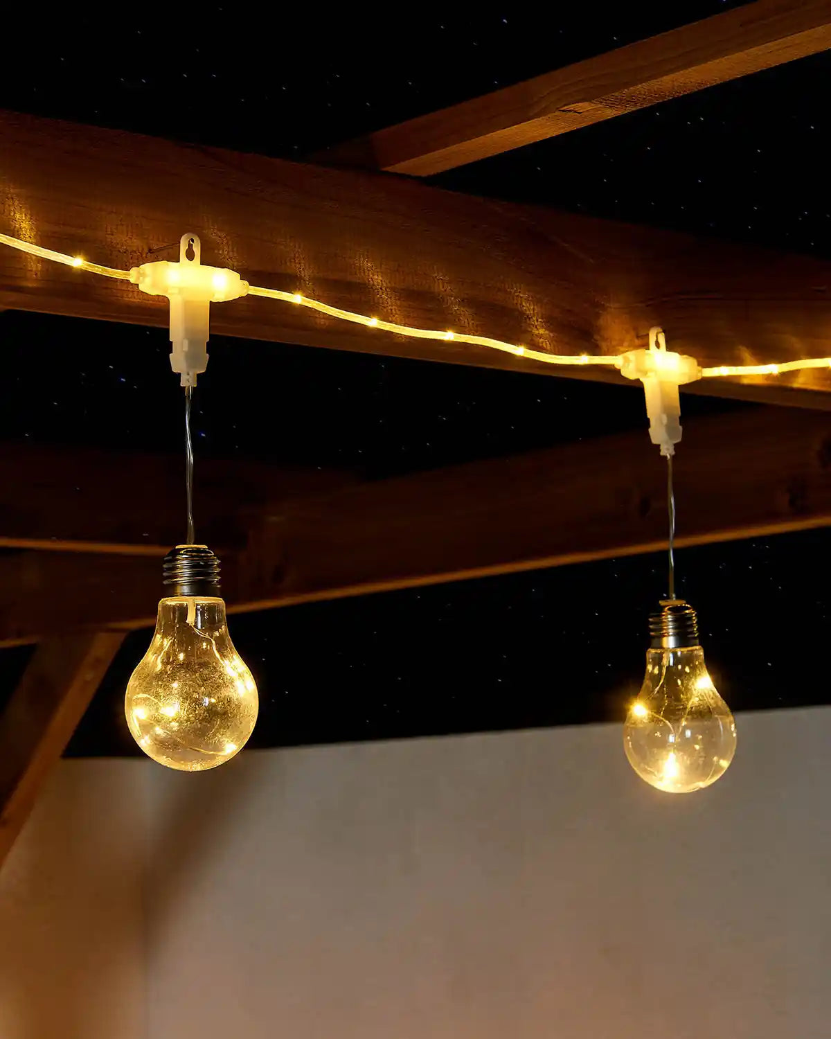 2 String lights with warm white glowing bulbs hanging from a wooden ceiling