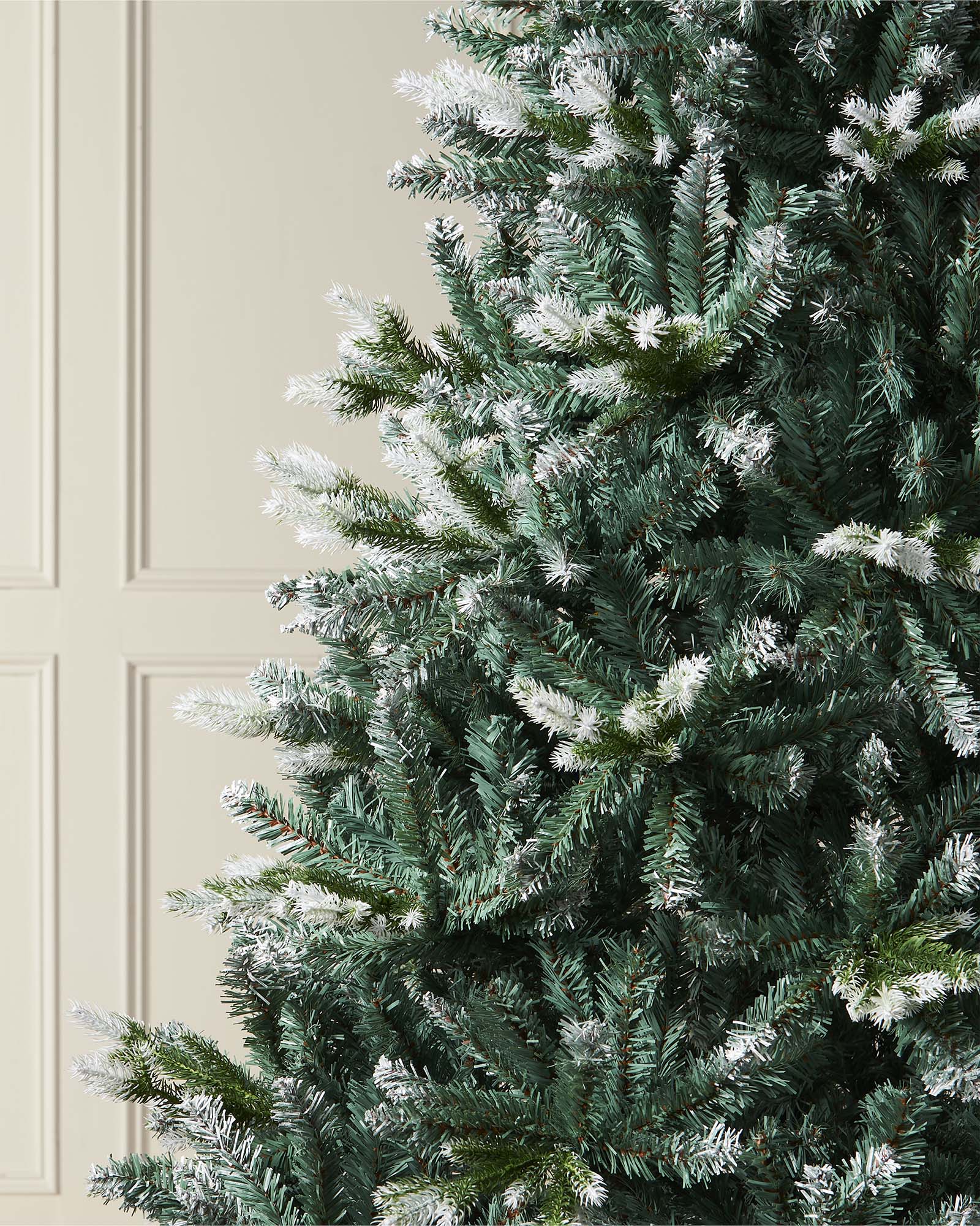 Life-like Evergreen Christmas tree with white snow-flocked tips and mixed cool green and blue tones, featuring hinged branches for easy assembly and storage—perfect for creating a trendy, rustic festive display indoors.