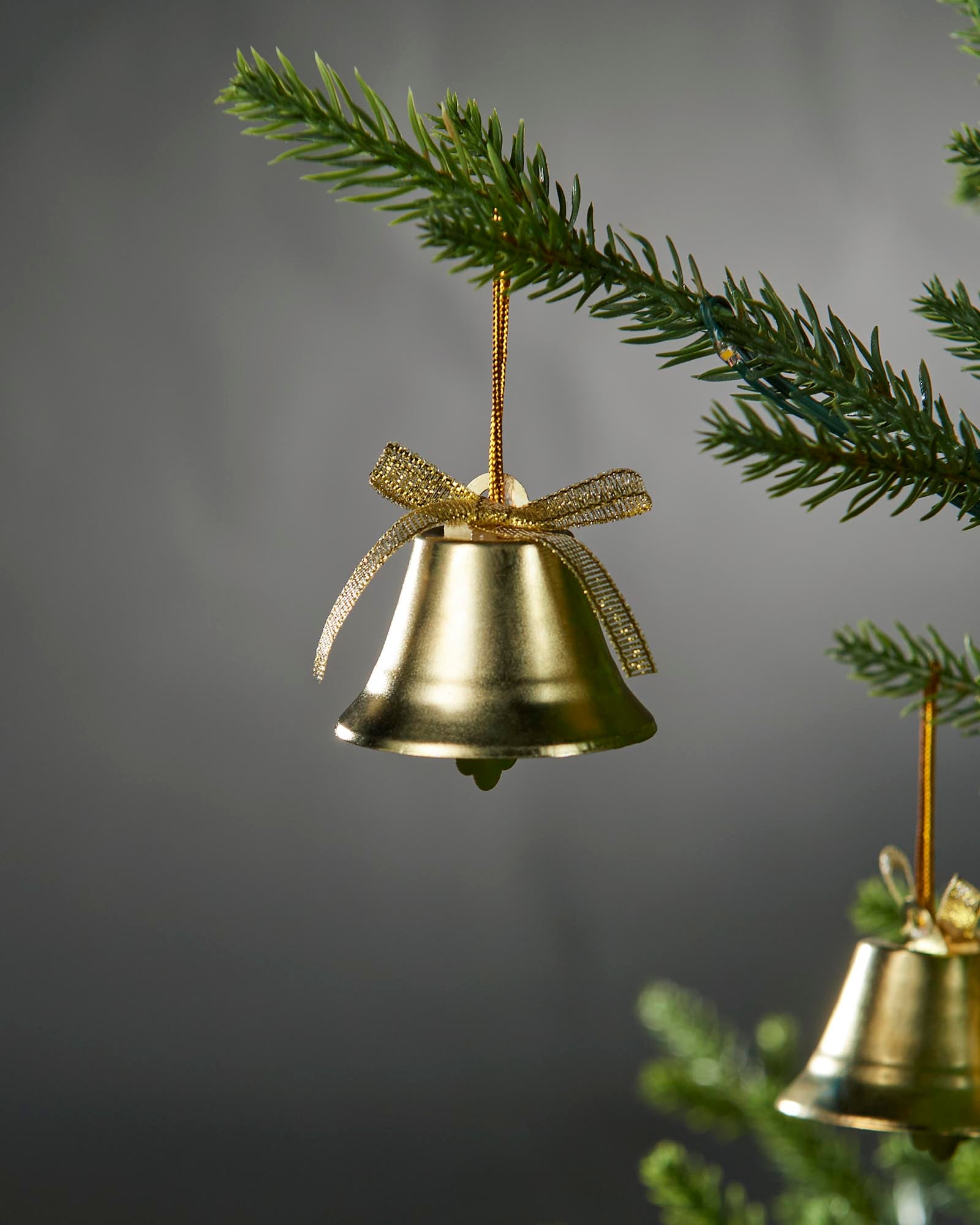 Gold bell ornament with a bow on a Christmas tree branch against a dark background