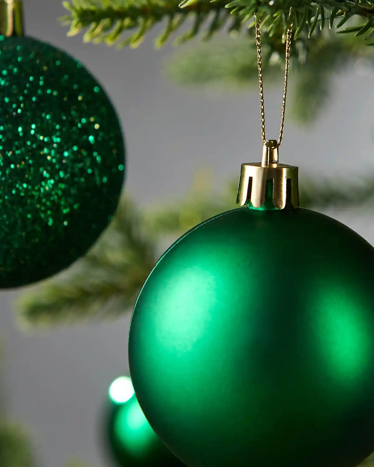 2 close up Green Christmas ornament hanging on a tree branch with a blurred background