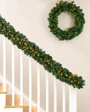 Christmas garland with lights draped over a staircase and a wreath on a wall.