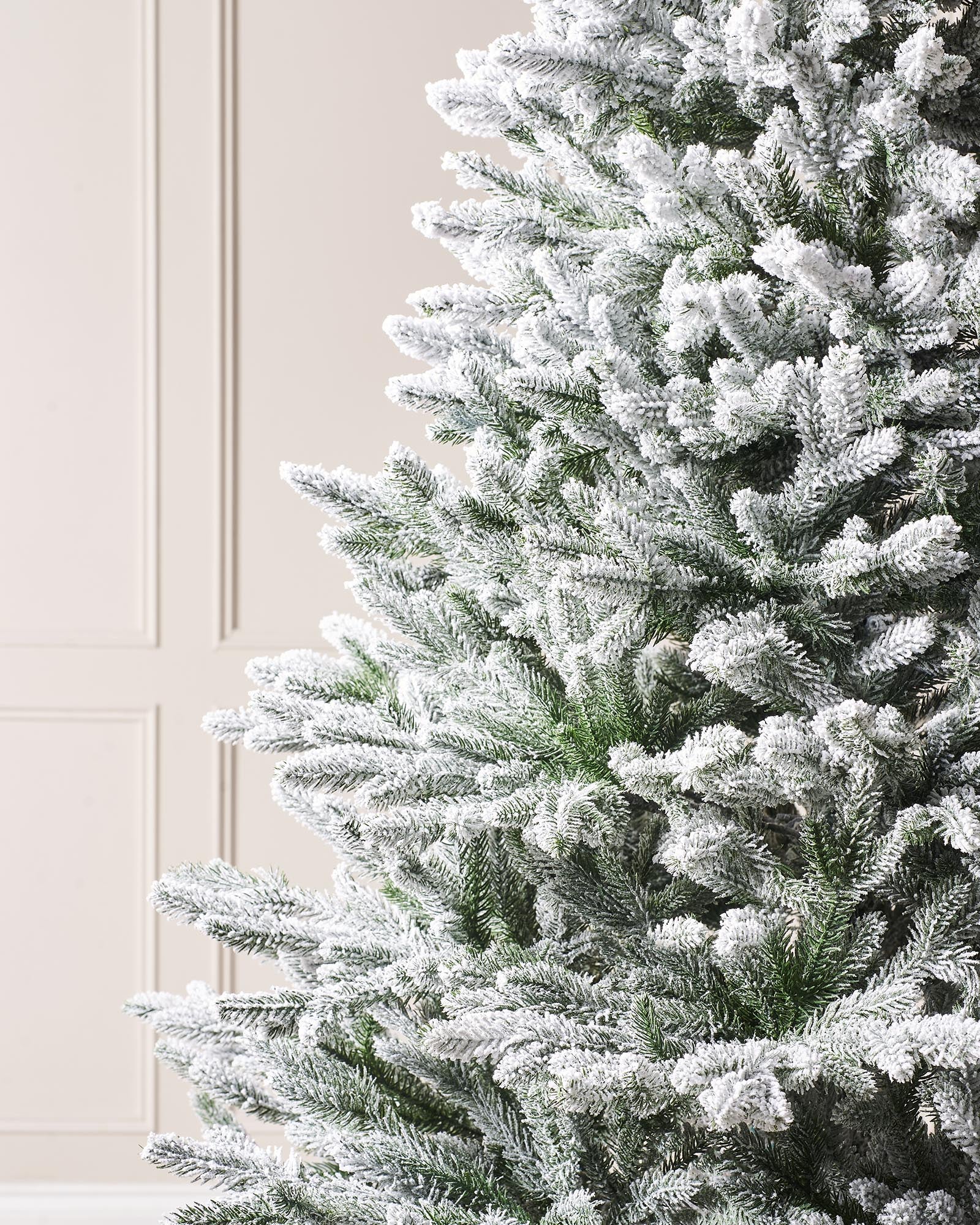 Luxury snow-flocked artificial Christmas tree with soft, snow-dusted tips and a full-bodied, naturalistic shape. Features hinged branches for easy assembly and storage, providing a reusable, elegant centerpiece that captures the charm of a rustic winter wonderland.