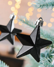 2 gloss Black star hanging baubles on a snow flocked Christmas tree with blurry lights in background 