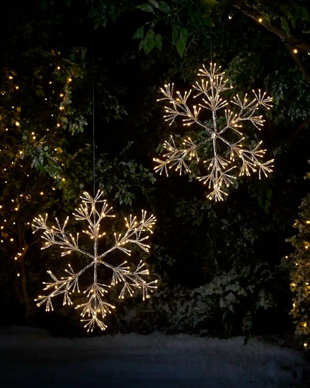 2 hanging snowflake LED Warn white silhouettes in a snowy garden setting