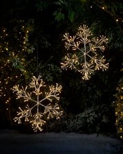 2 hanging snowflake LED Warn white silhouettes in a snowy garden setting
