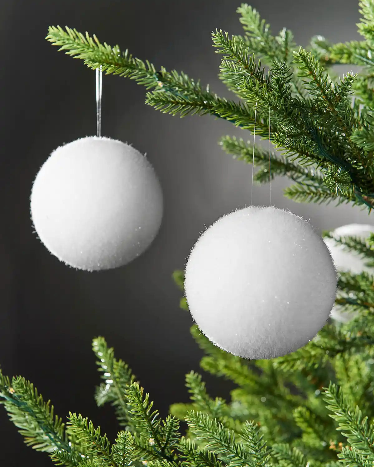 2 snowball baubles hanging on a Christmas tree branch against a Grey background