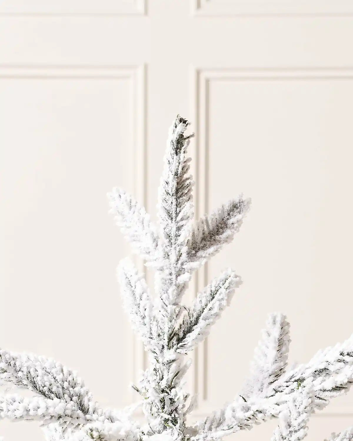 Close up of the Snow flocked tips on a 2ft Snow flocked artificial Christmas tree on a cream panel textured background
