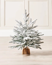 2ft Snow flocked artificial Christmas tree with a brown hessian-wrapped base on a cream panel textured background